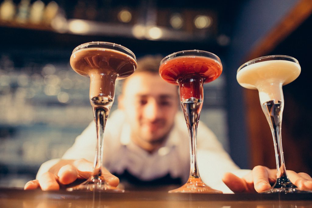  barman podający 3 kieliszki wypełnione drinkami - kurs robienia drinków