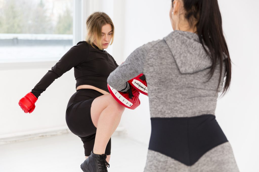 Zdeterminowana uczestniczka kursu samoobrony dla kobiet ćwiczy dynamiczne uderzenia na tarczy treningowej, budując siłę i pewność siebie.