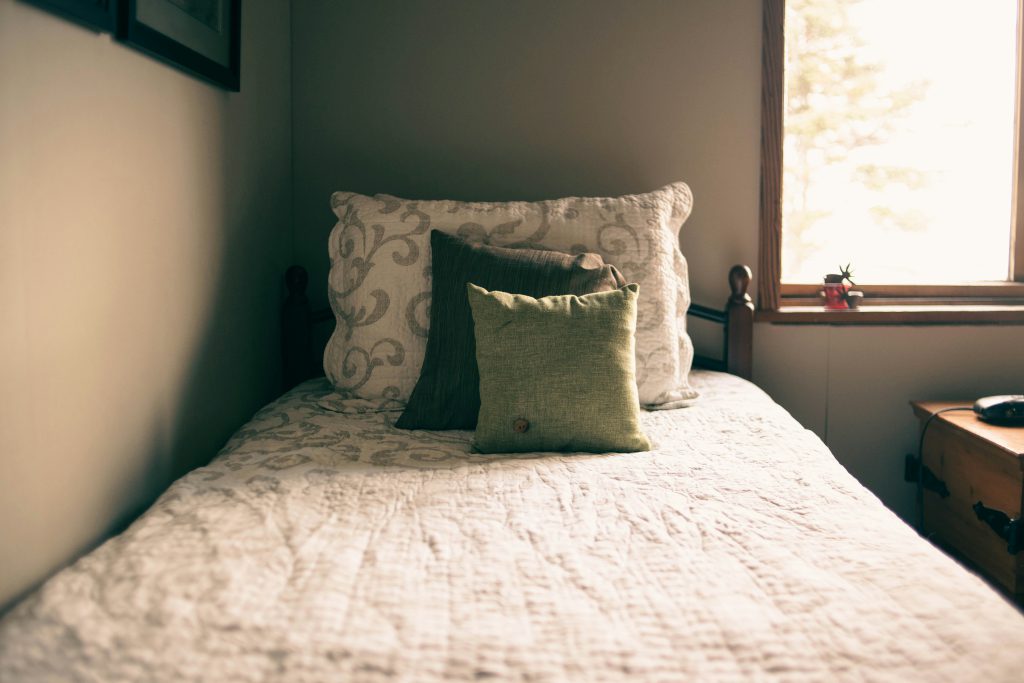 Na zdjęciu widoczne jest wąskie łóżko ustawione przy ścianie i oknie