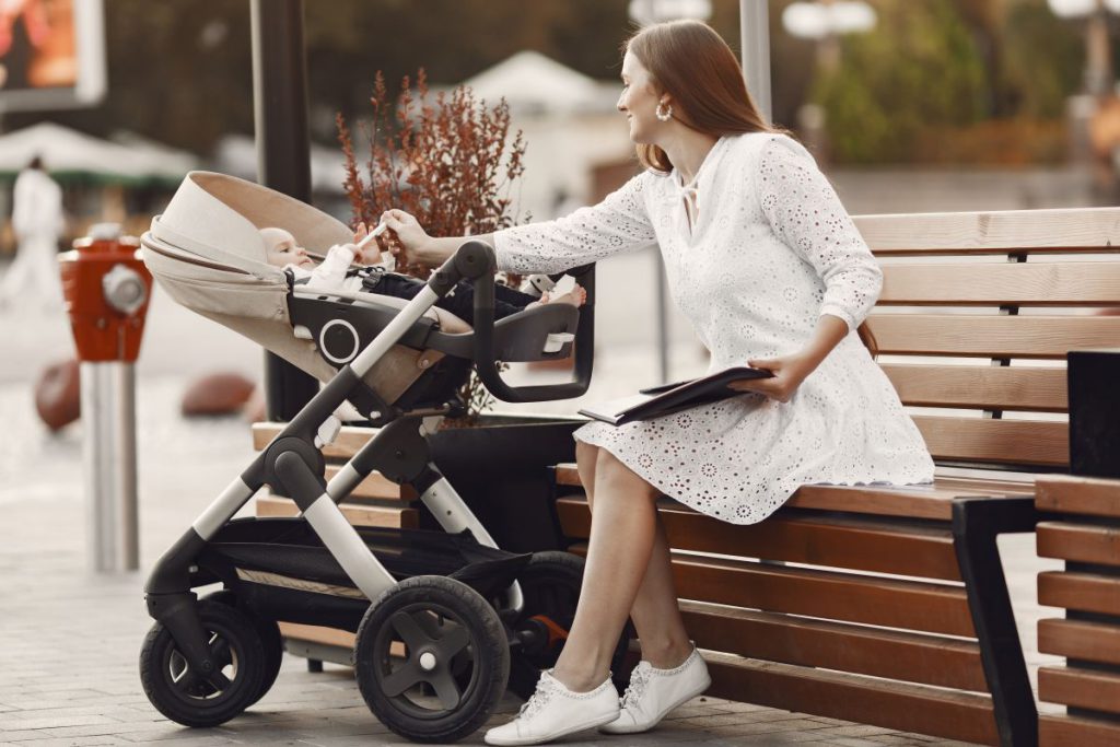 Młoda mama z nowoczesnym wózkiem dziecięcym odpoczywa na ławce